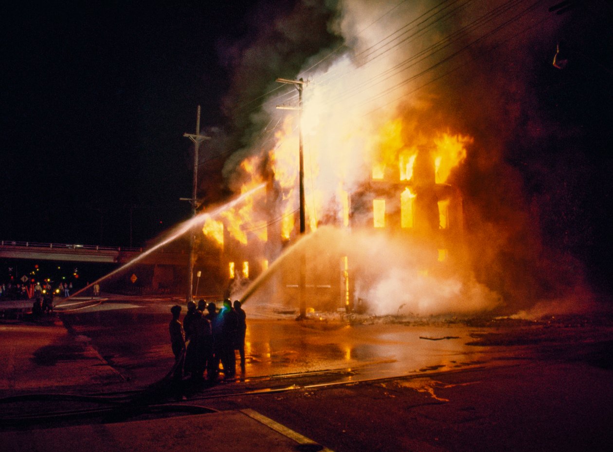 Um edifício urbano completamente tomado pelo fogo e pelas chamas, à noite, em Kansas City, com os bombeiros de Ted Spiegel
