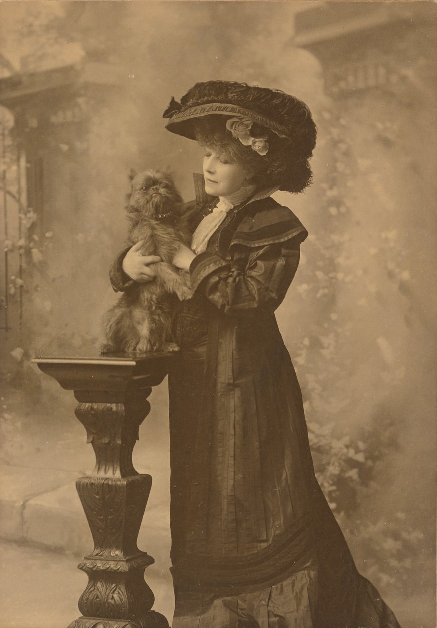 [Sarah Bernhardt de pé, num estúdio, segurando um pequeno cão preto sobre um pedestal de madeira entalhada ornamentado] de Theodore C. Marceau