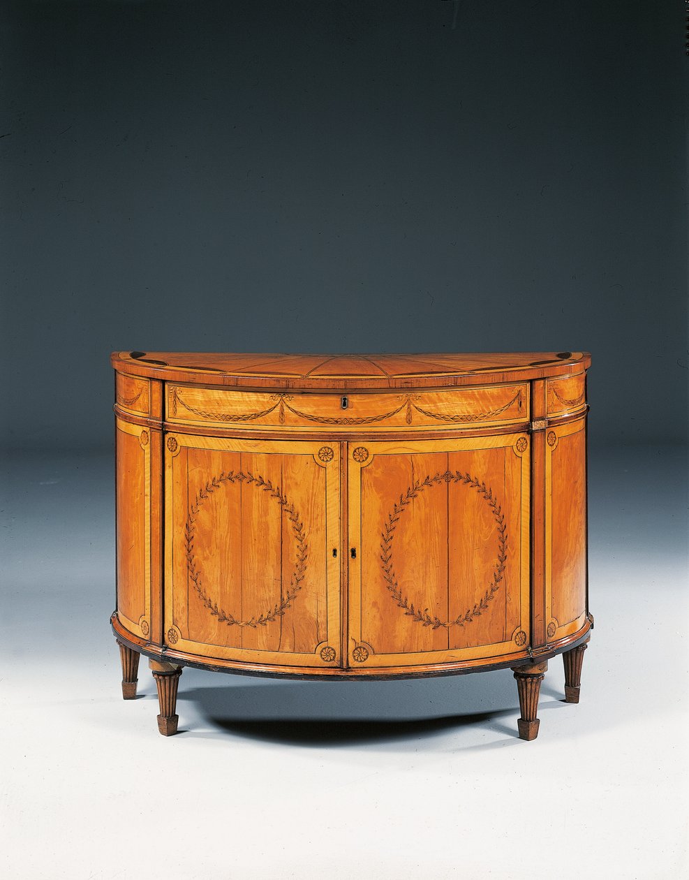 Cômoda de meia lua em marchetaria George III, c.1760-79 (madeira satin, amaranto e tulipwood) de Thomas (attr.to) Chippendale