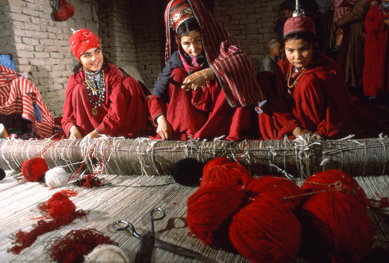 Mulheres de tribos turcomanas tecelãs cortam os nós da urdidura de um tapete num tear na aldeia de... de Thomas J. Abercrombie