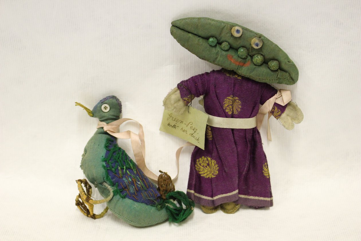 Boneca de trapos Miss Green Peas, a cabeça tem a forma de uma vagem de ervilha e conduz o seu pato de estimação por uma fita de cetim cor-de-rosa de Una Maw