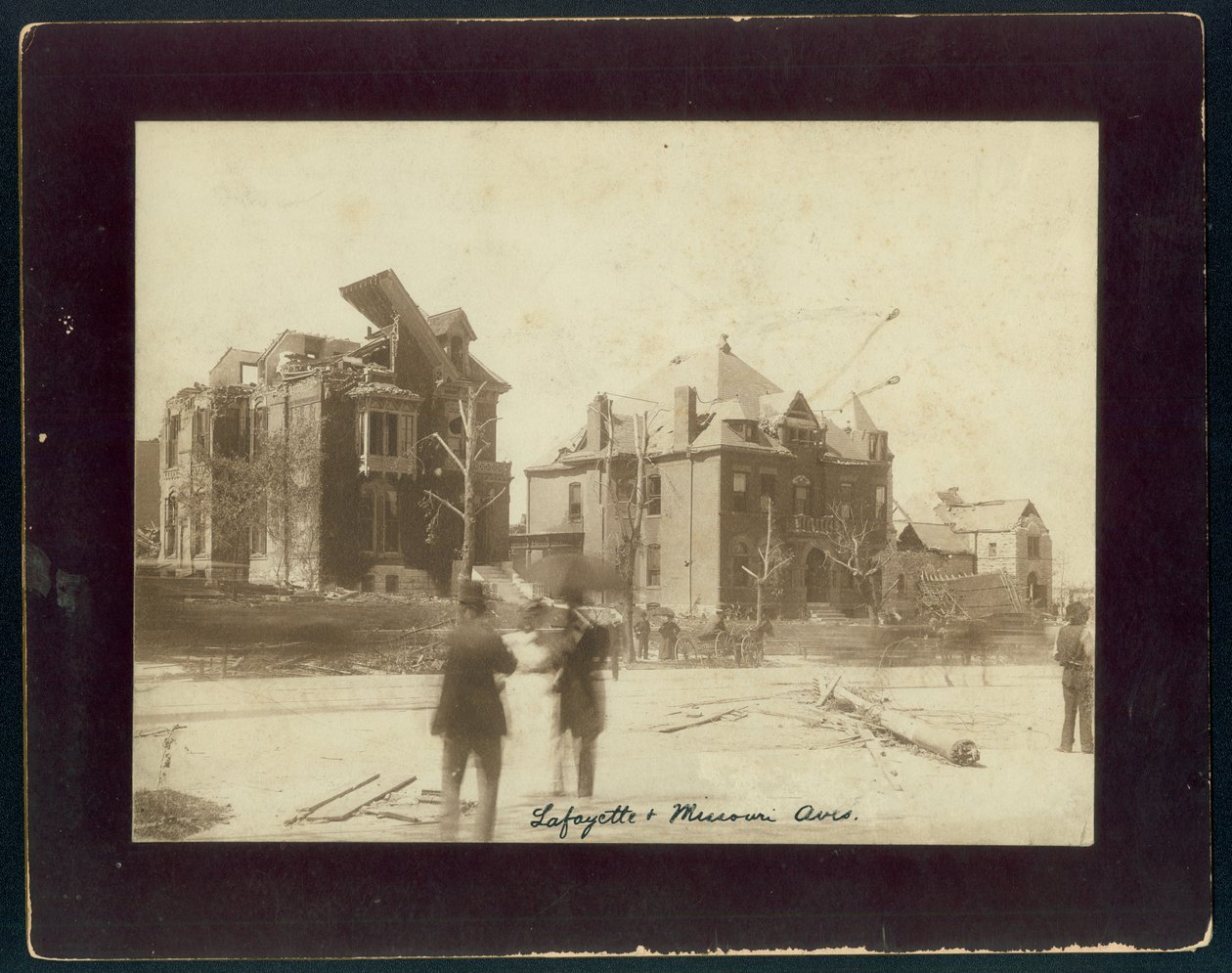 Foto horizontal em sépia mostrando três casas parcialmente destruídas, árvores despojadas e espectadores olhando para os danos resultantes de um tornado de Unbekannt Unbekannt