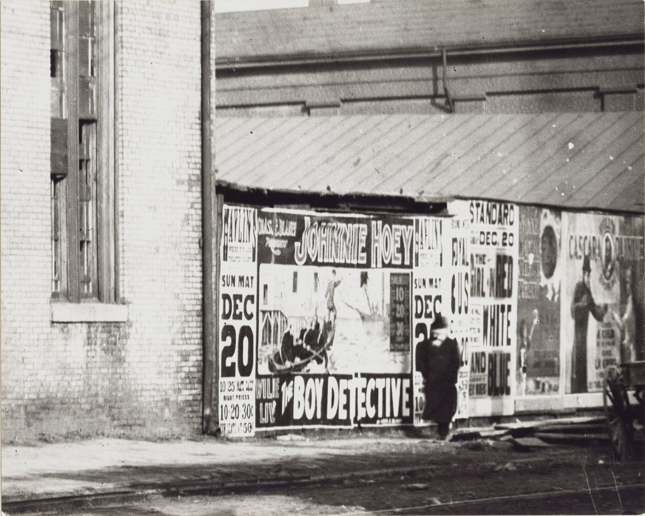 Um homem passa por uma parede de anúncios em pôster, incluindo um de Johnnie Hoey, o detetive do menino, no Havlin&39;s Theatre em Walnut Street, 600 de Unbekannt