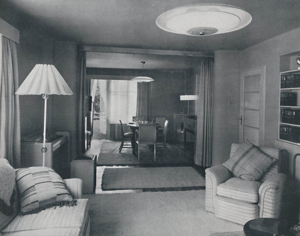 Sala de jantar e sala de estar, divididas apenas por cortinas pesadas em um atraente tecido moderno, 1942 de Unbekannt