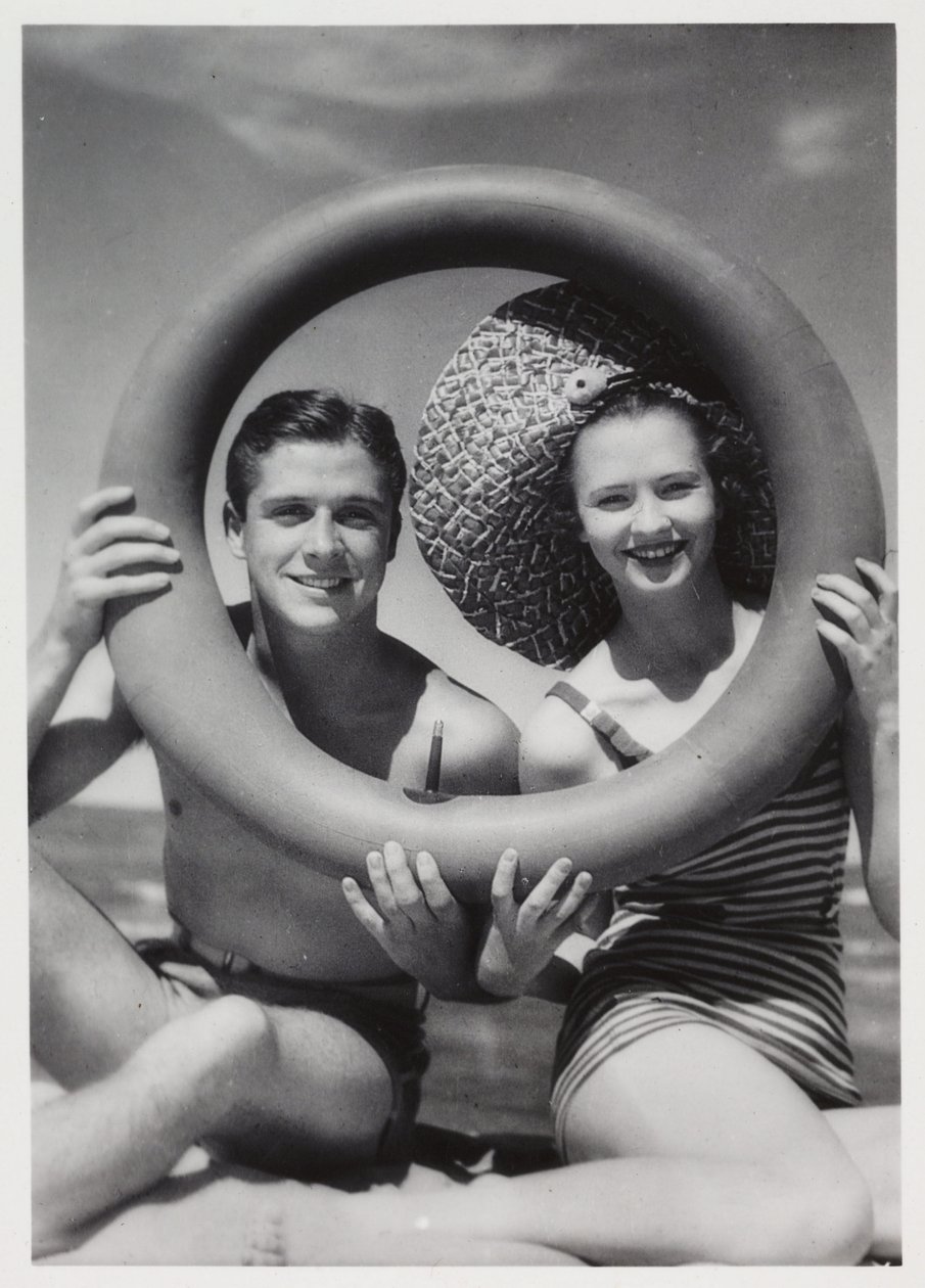 Homem e mulher olhando através de um anel de borracha na praia, c 1935 de Unbekannt