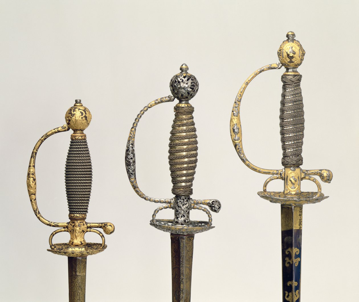 Punhos de três espadas francesas: uma de aço, azulada e recoberta de desenhos em ouro perseguido, c.1730; um de aço perfurado e cinzelado e o chão de ouro emaranhado, c.1760; um de aço cinzelado, gr de Unbekannt Unbekannt