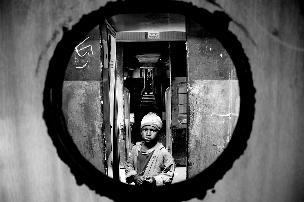 Retrato de uma criança da rua vista através do furo da porta do compartimento de um trem na estação de trilho de Kamalapur em Dhaka, Bangladesh. 5 de janeiro de 2007. de Unbekannt Unbekannt
