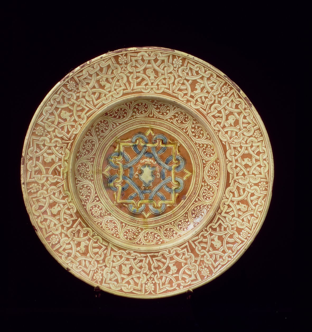 Placa Maiolica decorada com um elaborado desenho de nó repetitivo emoldurando cabeças de perfil na borda e um escudo na placa central, italiana, feita na Toscana de Unknown