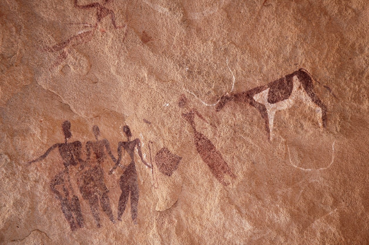 Arte rupestre, Pré-história: Pintura rupestre de um grupo de personagens e uma vaca de duas cores com chifres grandes num abrigo ornamentado, no maciço de Uweinat, Egipto. (Período de 8000 a 3000 anos a.C.). Fotografia de Unbekannt