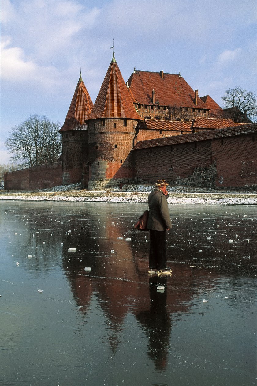 Perfil lateral de um homem em pé num rio congelado em frente a um castelo, Rio Nogat, Castelo de Malbork, Malbork, Província de Pomorskie, Polónia de Benjamin Baud