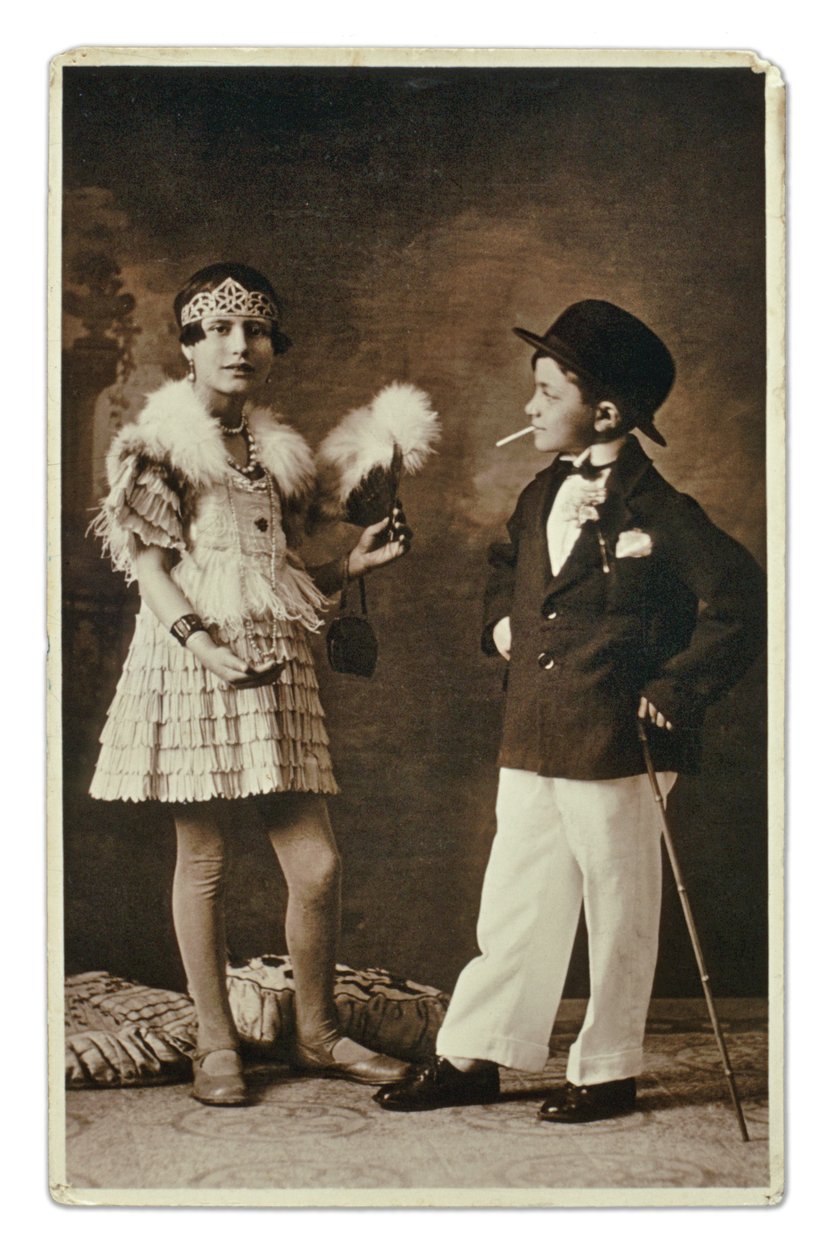 Duas crianças vestidas como um adulto à moda dos anos 20, a menina com um fato de Charleston, e ele de fato, chapéu de coco e cigarro. Fotografia de Unbekannter Künstler
