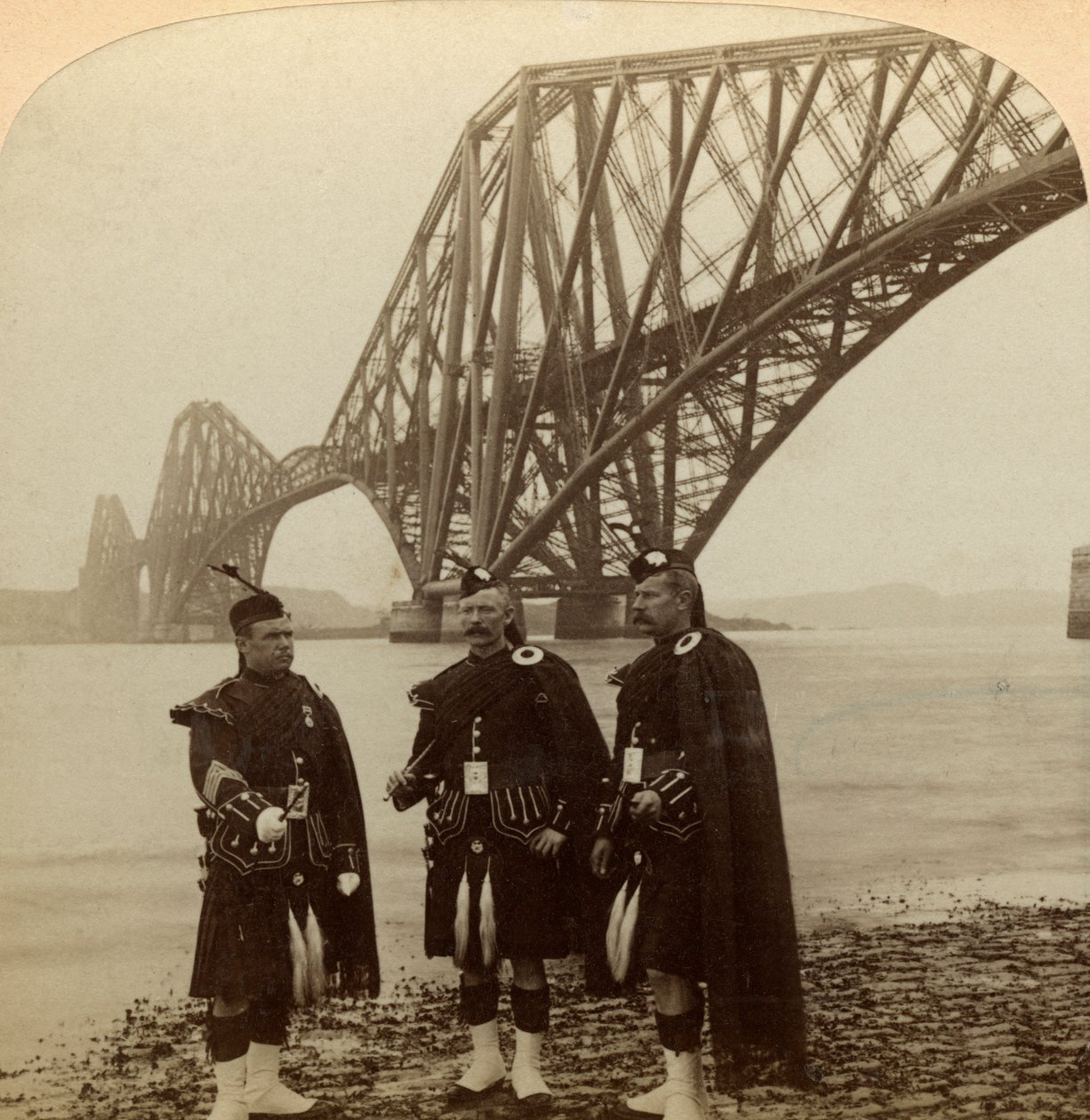 Homens de Highland se vestem em frente à Forth Bridge, na Escócia. de Underwood and Underwood