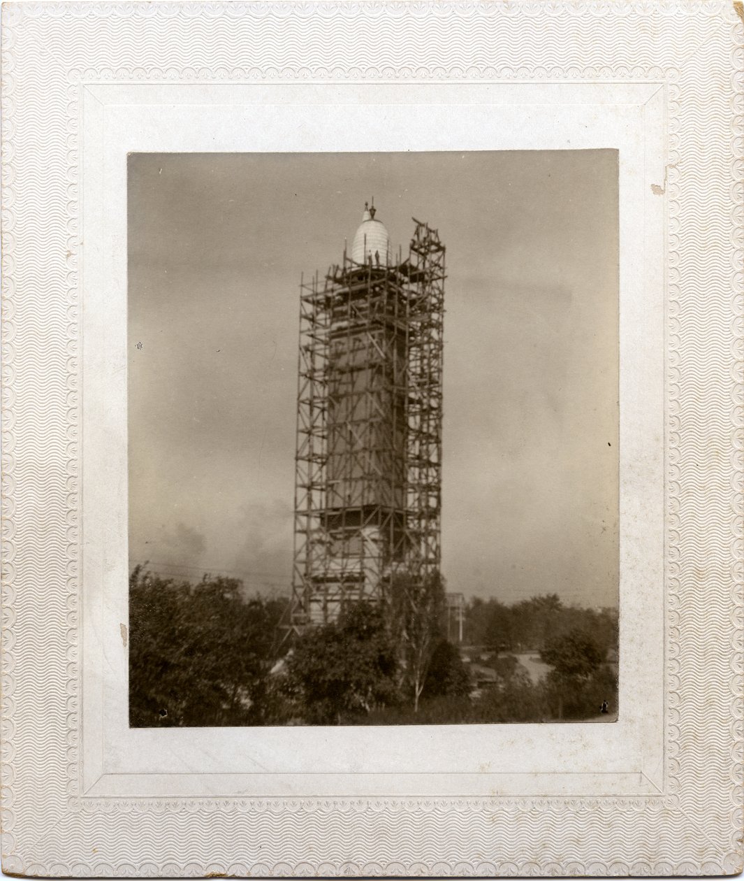 Construção da Torre de Água Compton Heights sobre o standpipe existente, com andaimes ao redor da torre e trabalhador no nível do telhado. de Unknown