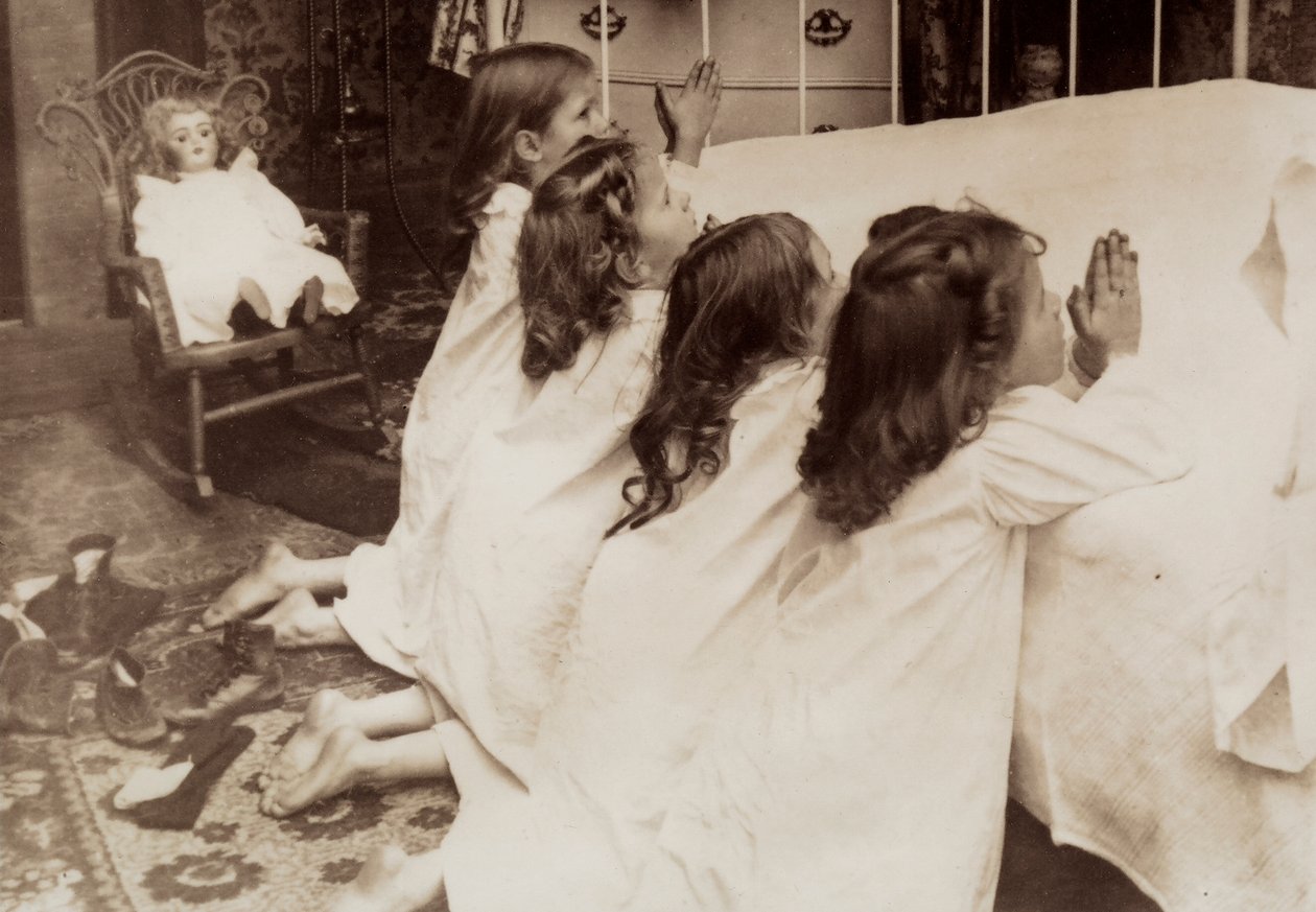 Quatro meninas ajoelhadas ao lado de uma cama enquanto rezam a oração da noite. de Unknown photographer