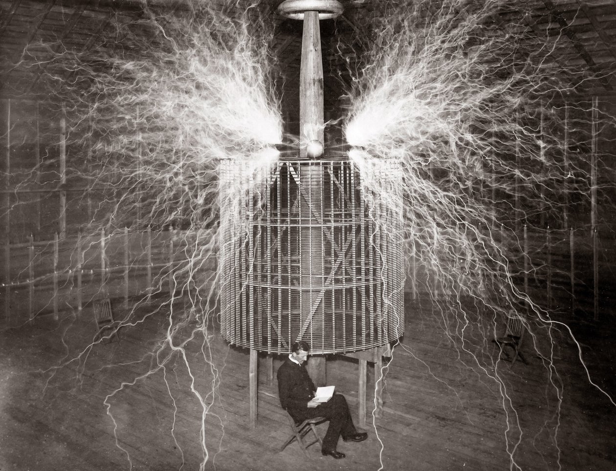 Nikola Tesla sentado no seu laboratório em Colorado Springs com o seu "Transmissor de Ampliação" de Unknown photographer