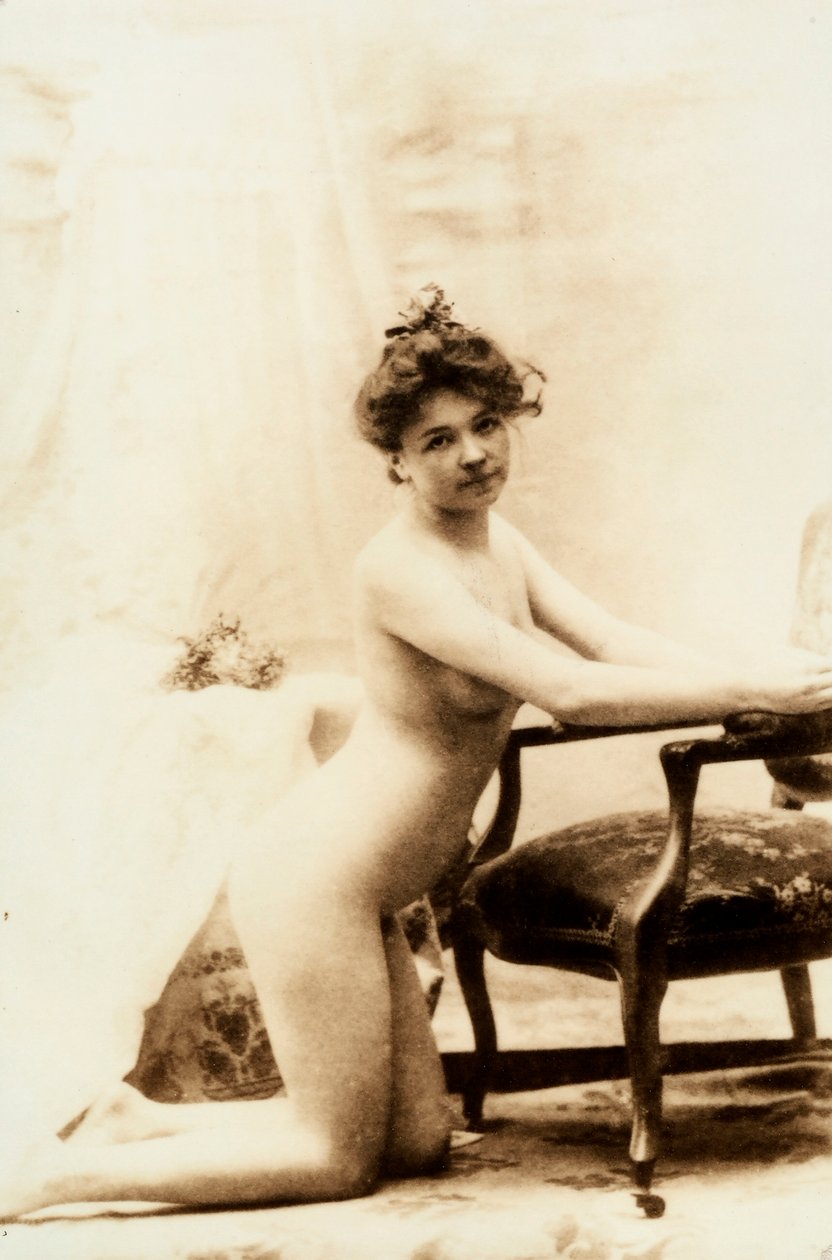 Retrato nu de uma jovem mulher ajoelhada em frente a uma pequena poltrona. de Unknown photographer
