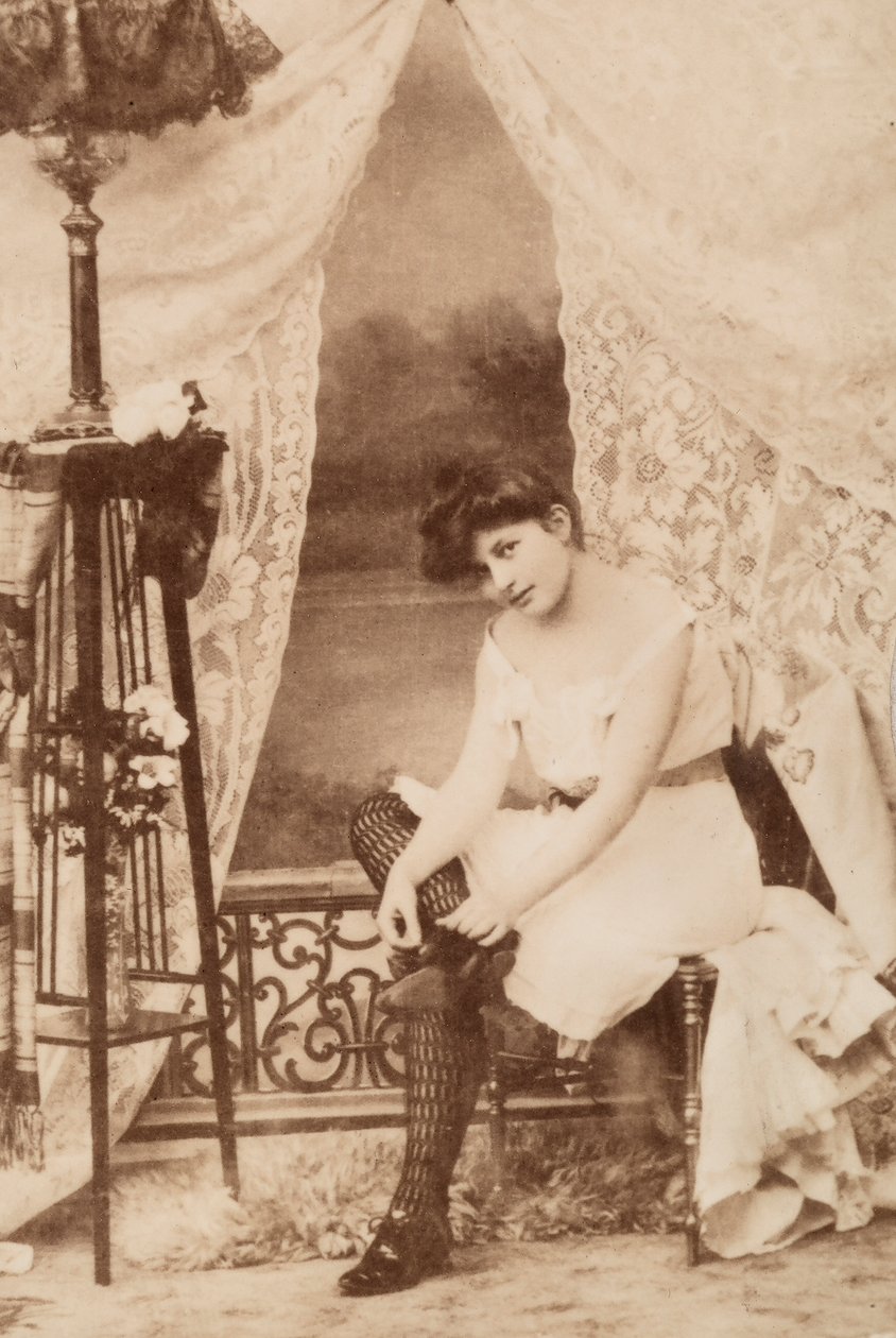Retrato de uma jovem mulher em trajes íntimos, sentada enquanto ata o seu sapato. de Unknown photographer
