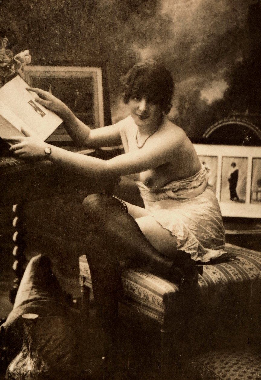 Retrato de uma jovem mulher em trajes íntimos, sentada a uma mesa com um livro. de Unknown photographer