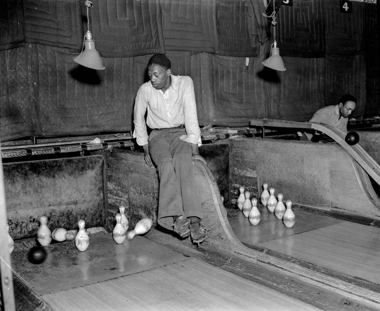 Um homem afro-americano que vai a dez pinos numa pista de bowling, para repor manualmente o pino... de Volkmar Wentzel