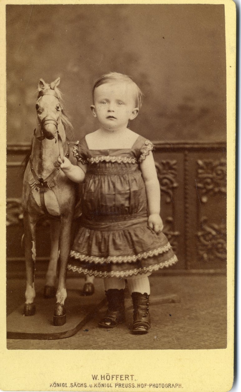 Menina de pé ao lado de um cavalo de balanço de W. Hoffert