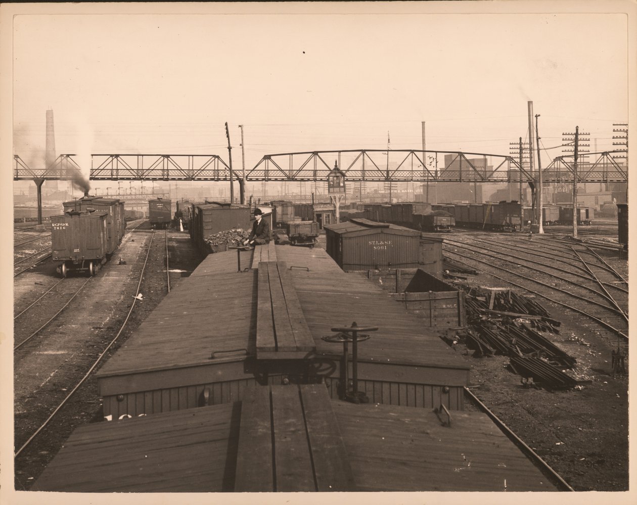 Fotografia horizontal, preto e branco de vagões ferroviários em um pátio ferroviário. Um homem senta em cima de um dos carros de William G. Swekosky