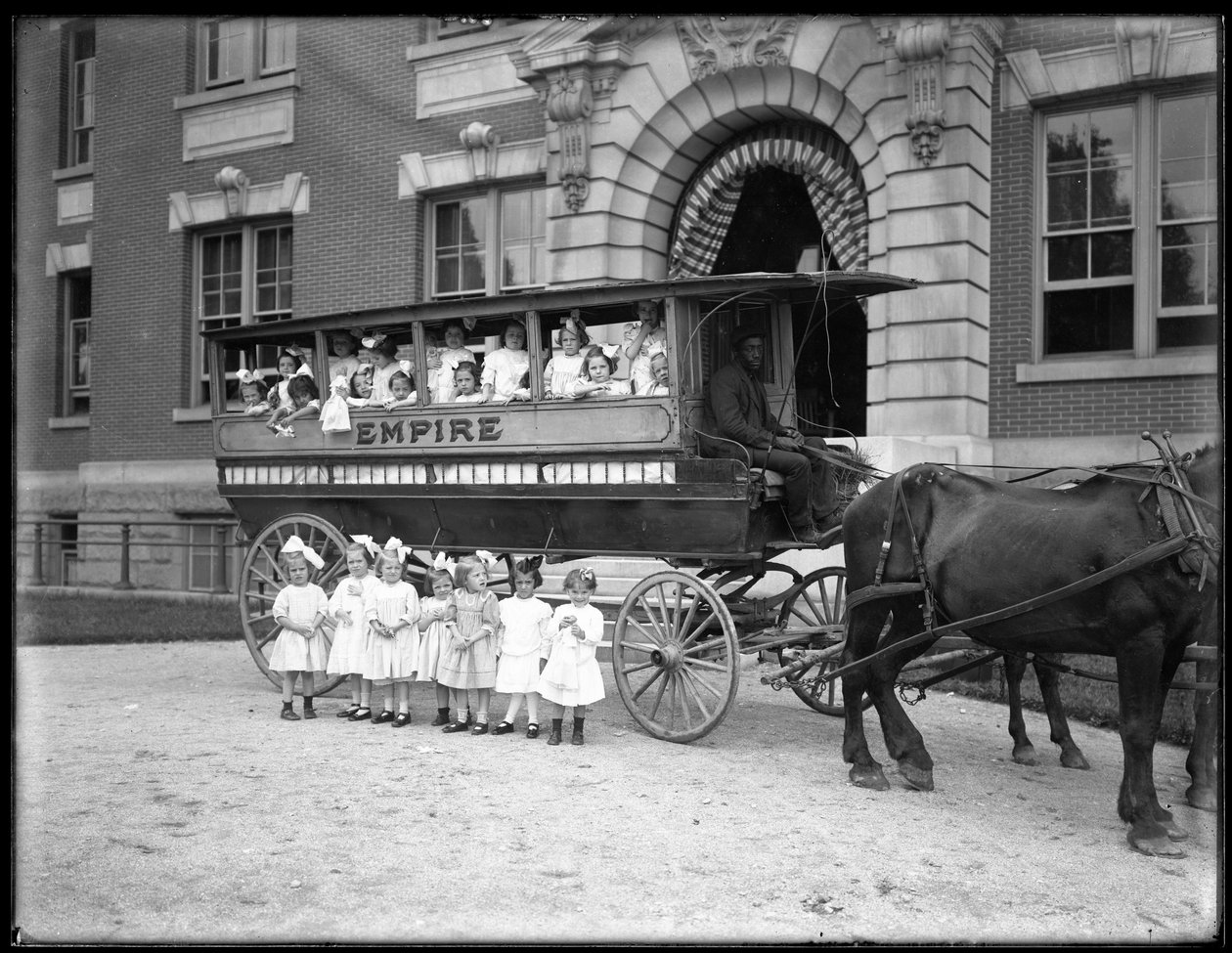 As meninas pequenas colocam dentro e na frente de um vagão puxado por cavalos, na frente de um edifício não identificado, provavelmente o asilo órfão católico romano, Kingsbridge, Bronx, c.1910 de William Davis Hassler