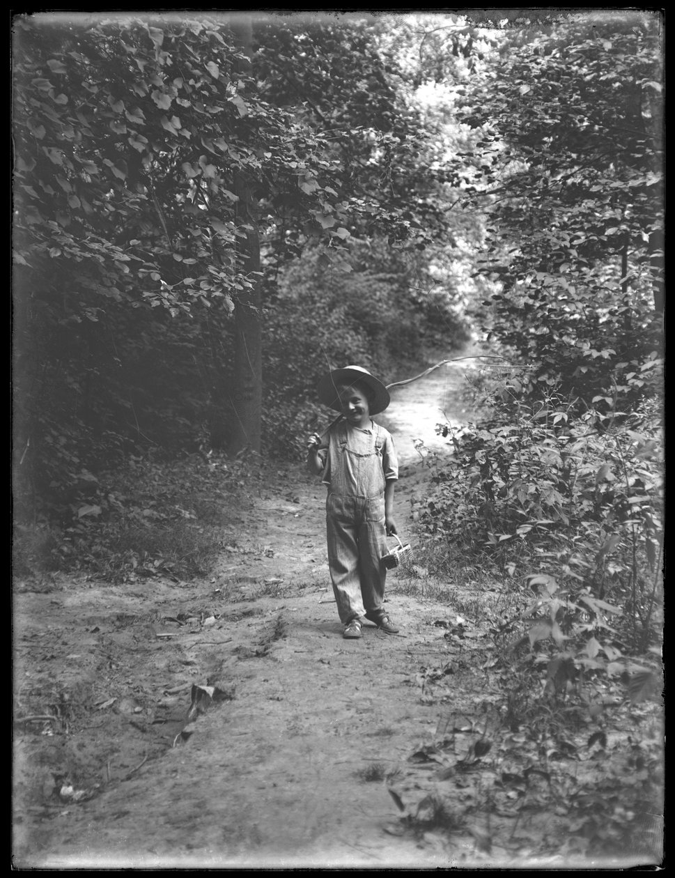 William Gray Hassler de chapéu de palha e macacão, carregando vara de pescar e cesto, andando sozinho por um caminho no bosque, 20 de agosto de 1911 de William Davis Hassler