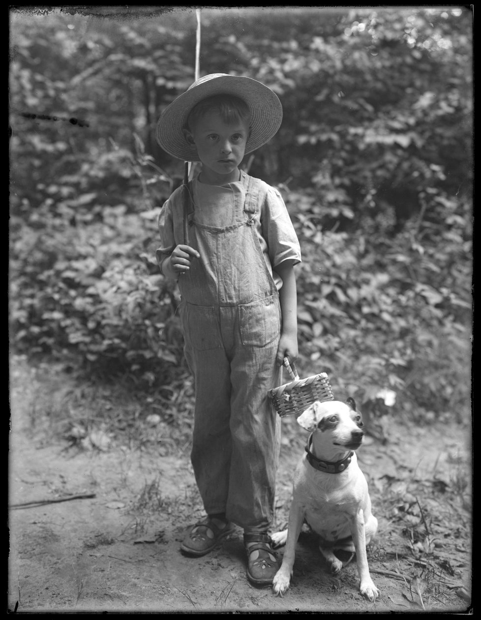 William Gray Hassler de chapéu de palha e macacão, carregando vara de pescar e cesta, posou na floresta com um cachorro pequeno (Bessie), 20 de agosto de 1911 de William Davis Hassler