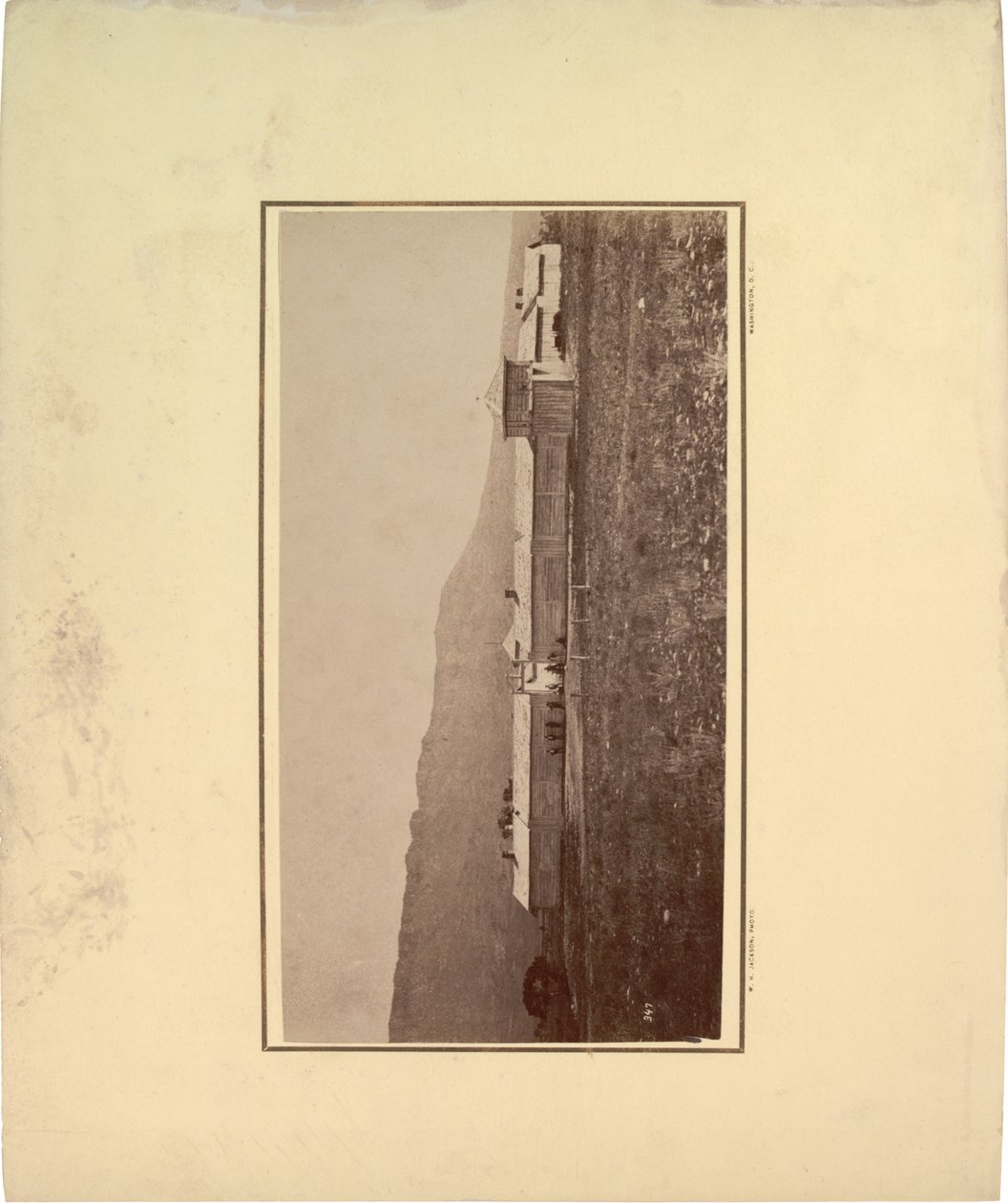 Vista de uma paliçada com vários homens reunidos no portão de entrada, 1871 (foto sépia) de William Hicks Jackson