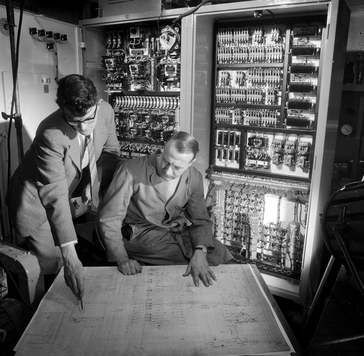 Engenheiros discutem planos em frente ao painel de controle eletrônico que construíram de Frederick (attr. to) Barnard