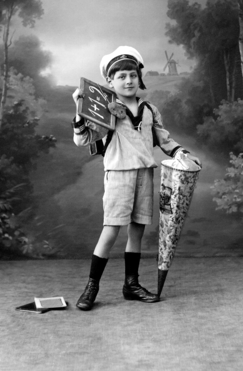 Primeiro dia de aulas. Um jovem rapaz de uniforme posando com uma ardósia mostrando a adição 1+1 = 2 e uma bolsa surpresa. Fotografia por volta de 1910. de Ferdinand Georg Waldmuller