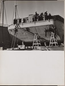 [Um grupo de homens trabalha num barco atracado].
