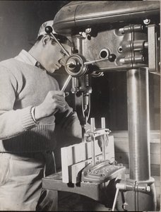 [Homem utiliza uma máquina para fazer furos em dois blocos de madeira].