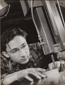 [Homem de óculos trabalha atentamente com um ficheiro industrial] de Arnold Eagle