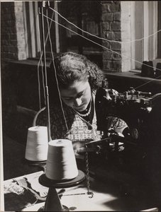 [A mulher utiliza uma máquina de costura com dois carretéis de linha branca]. de Arnold Eagle