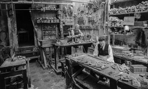 Artesãos numa bancada de trabalho numa oficina a fabricar pequenos objectos de madeira que não parecem...