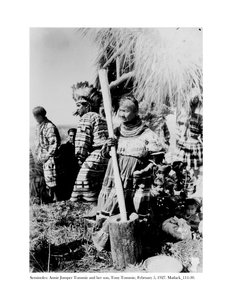 Annie Jumper Tommie usando um almofariz e um pestel para fazer farinha de milho, e seu filho, Tony Tommie, usando um chapéu de penas de águia, 5 de fevereiro de 1927