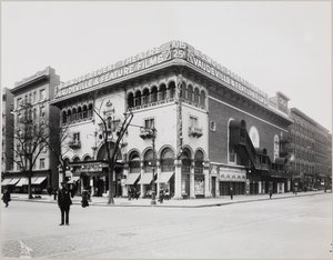 Um teatro enorme com uma fachada elaborada, completo com arcos e varandas mouriscas. Uma grande placa no topo do edifício diz "B.S. Moss Regent Theatre Vaudeville & Feature Films". Uma placa publicitária de Olga Petrova em "O Coração de uma Mulher Pintada"
