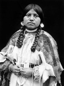 Mulher Cayuse, retrato de meio comprimento, de pé, virada para a frente, tranças, brincos de disco de concha, estrangulador de contas de concha e contas de concha à volta do pescoço, vestido de pele de musselina com cinto de contas c. 1910, foto Edward S.  de Edward Sheriff Curtis