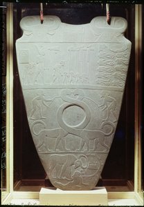 A Paleta Narmer: paleta cerimonial que representa o Rei Narmer, usando a coroa vermelha do Baixo Egito, inspecionando prisioneiros presos e decapitados, também um par de gigantescos gatos de pescoço comprido, encontrados em Hieraco