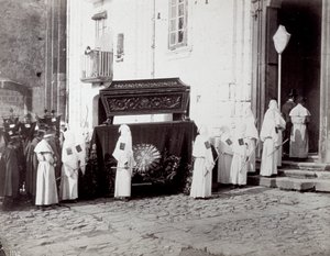 Procissão fúnebre da Congregação de São Francisco em Nápoles. Em primeiro plano, em frente a uma igreja, numerosos "irmãos confrarias" em túnicas e capuzes brancos acompanham um catafalque decorado com um pano bordado no qual é colocado o caixão. de Giorgio Sommer