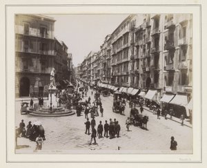 Vista da Via Roma, em Nápoles, com uma estátua, lojas, carruagens puxadas por cavalos e transeuntes