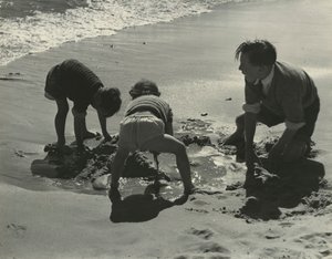 Três crianças a brincar com areia na praia.