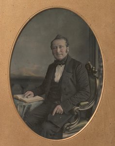 Homem sentado apontando para uma passagem em um livro aberto, década de 1850.