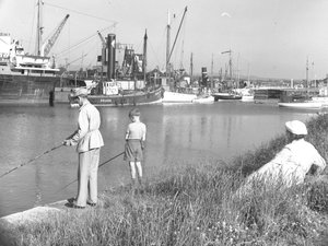 Um homem e um rapaz a pescar na doca de Glasson enquanto uma senhora marinha; paisagem marítima; ted atrás olha, vários barcos atracados de Joseph Hardman
