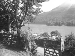 Quatro pessoas sentadas num muro de pedra seca a fazer um piquenique com vista para o lago, o carro estacionado com a bagageira aberta de Joseph Hardman