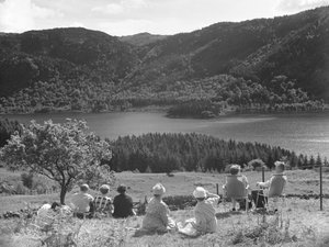 Grupo de pessoas sentadas na relva ou em espreguiçadeiras com vista para Thirlmere de Joseph Hardman