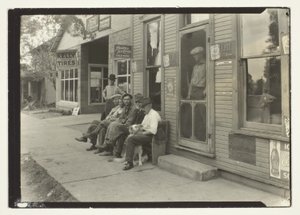 Homens com cão sentados num banco em frente a um armazém geral de Lewis Wickes Hine