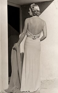 Modelo vista de trás usa vestido de noite da casa de alta costura "Fumach". O artigo deixa as costas nuas e é adornado com um alfinete com jóias. (foto a p/b)