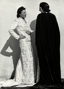 Dois modelos apresentam criações da casa de alta costura italiana "Dragoni". Um modelo veste uma roupa em material fralda composta por uma jaqueta e saia comprida com trem. O outro modelo, visto de trás, veste um longo manto de veludo. (foto a p/b) de Luis Bogino